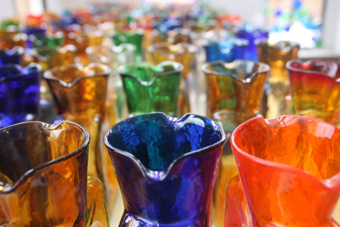 Close-up of vibrant, hand-blown glass vases in a variety of colors, showcasing artisan craftsmanship and decorative glass art in a well-lit display.